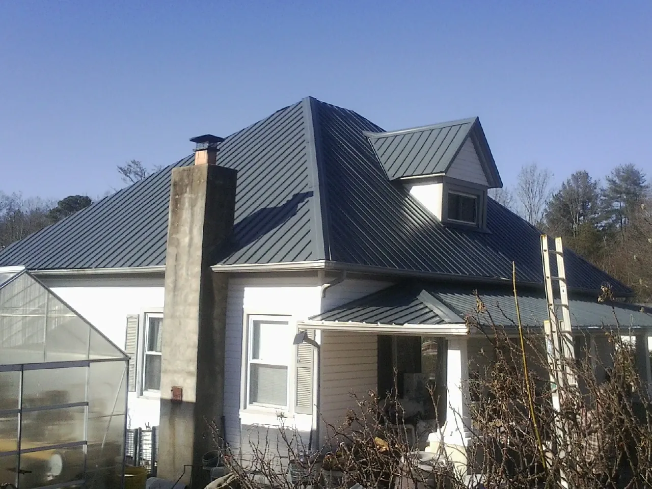Dark blue standing seam metal roof on a white farmhouse with dormer — Slate & Tile Roof Repair by Roofing Brothers in Horntown