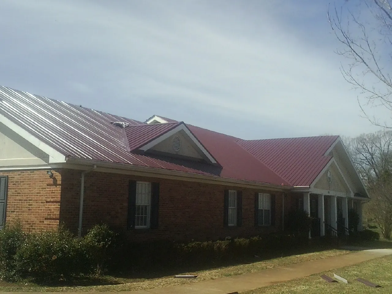 Red metal roof with gabled entries on a long brick building, from a Hail Damage Roof Repair job in Horntown