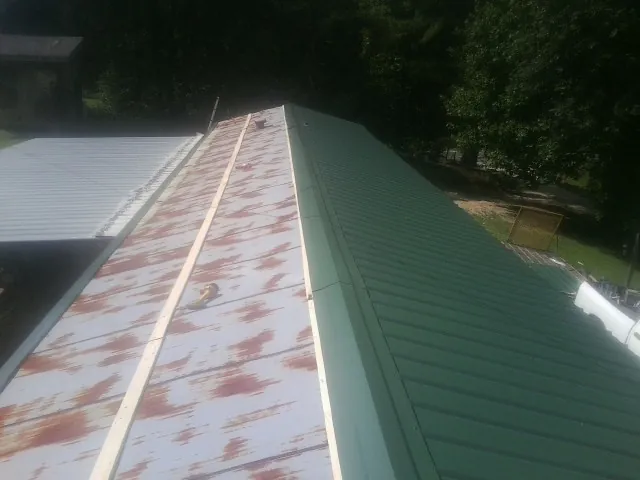 Old rusted panels beside newly installed green metal roofing — Wind Damage Roof Repair by Roofing Brothers in Horntown