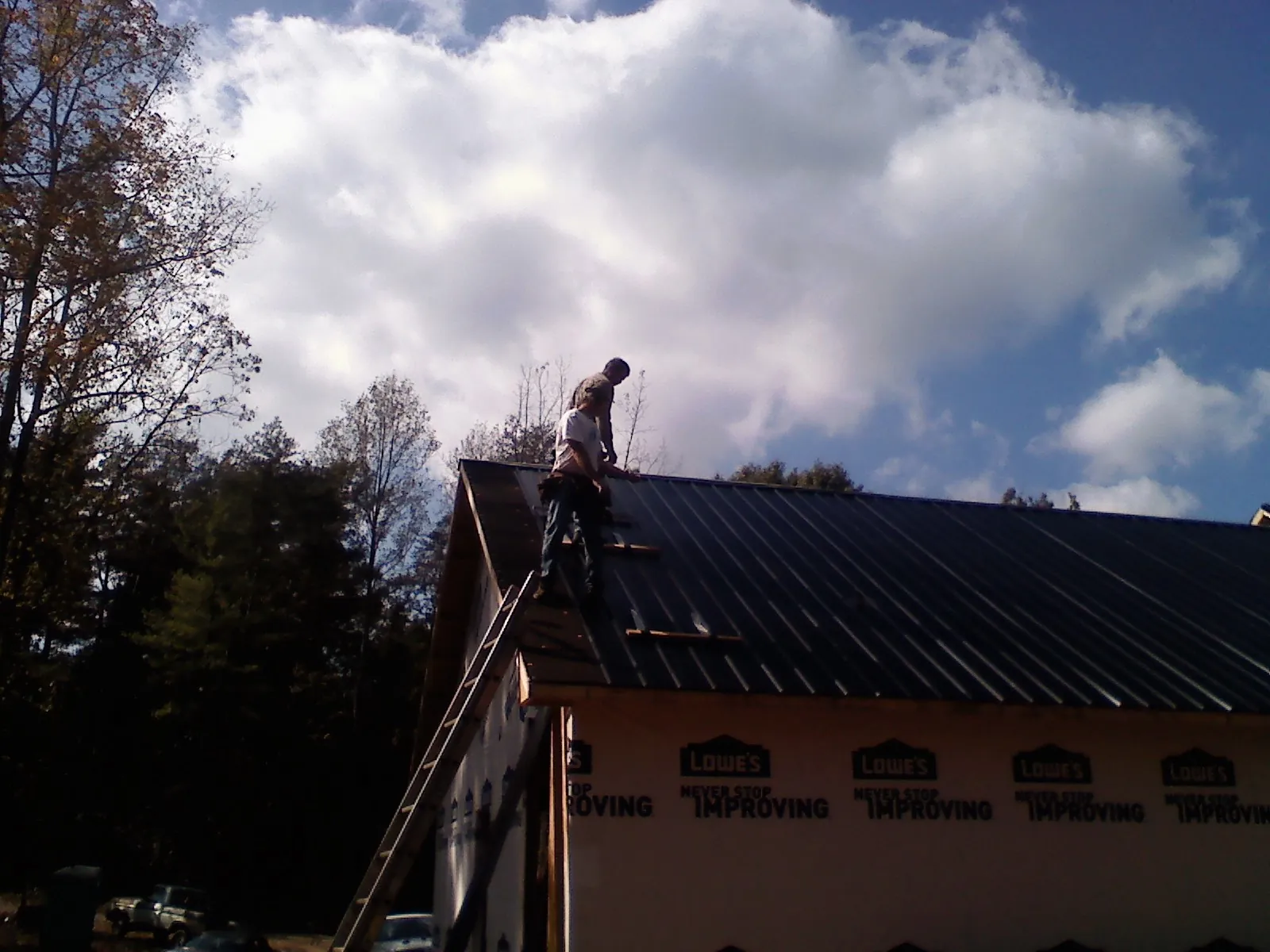Roofer fastening dark metal panels high against a cloudy sky, from a Roof Inspection job in Horntown