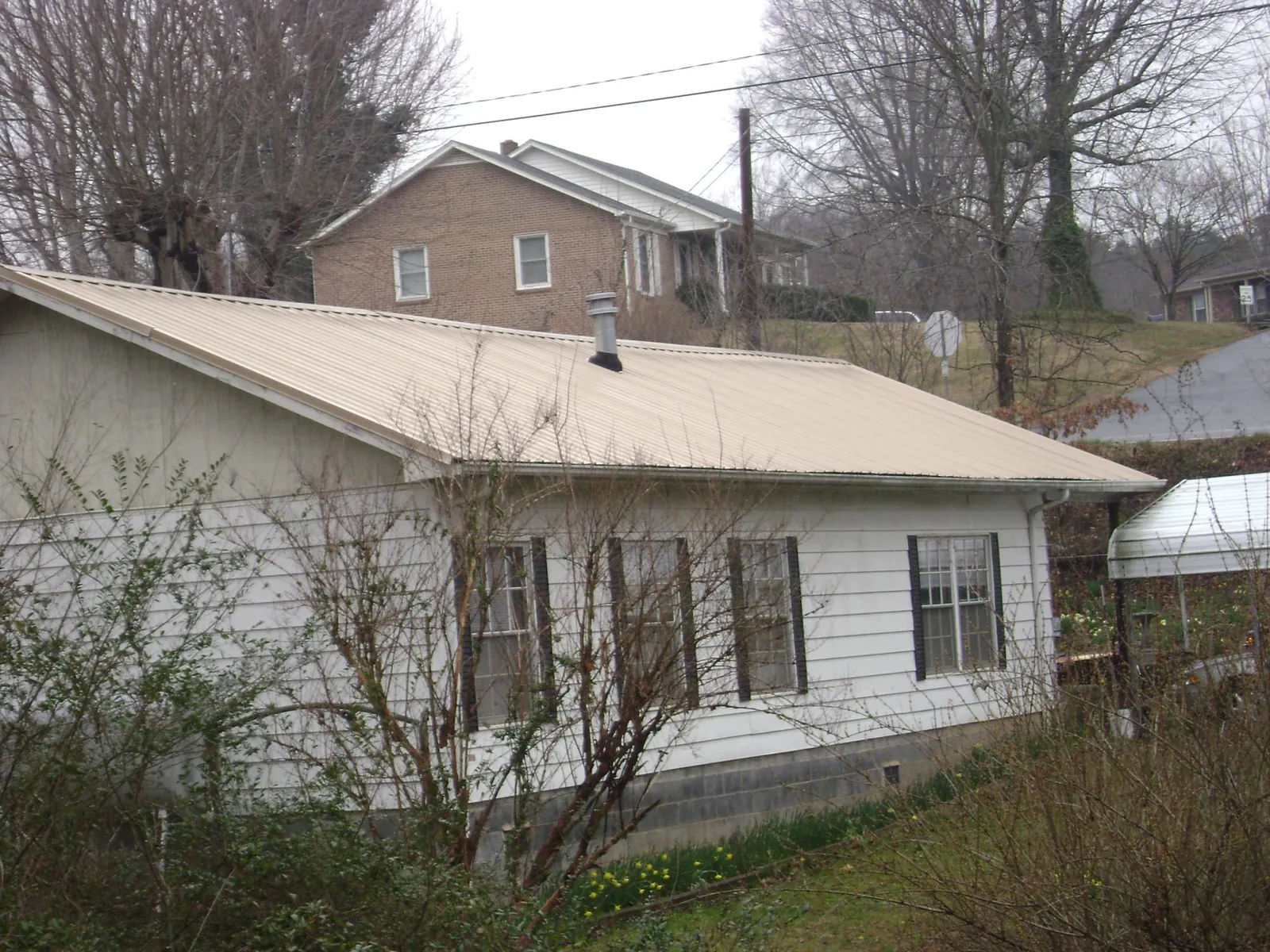 Tan metal roof on a white sided house set into a hillside — Commercial Roofing by Roofing Brothers in Horntown