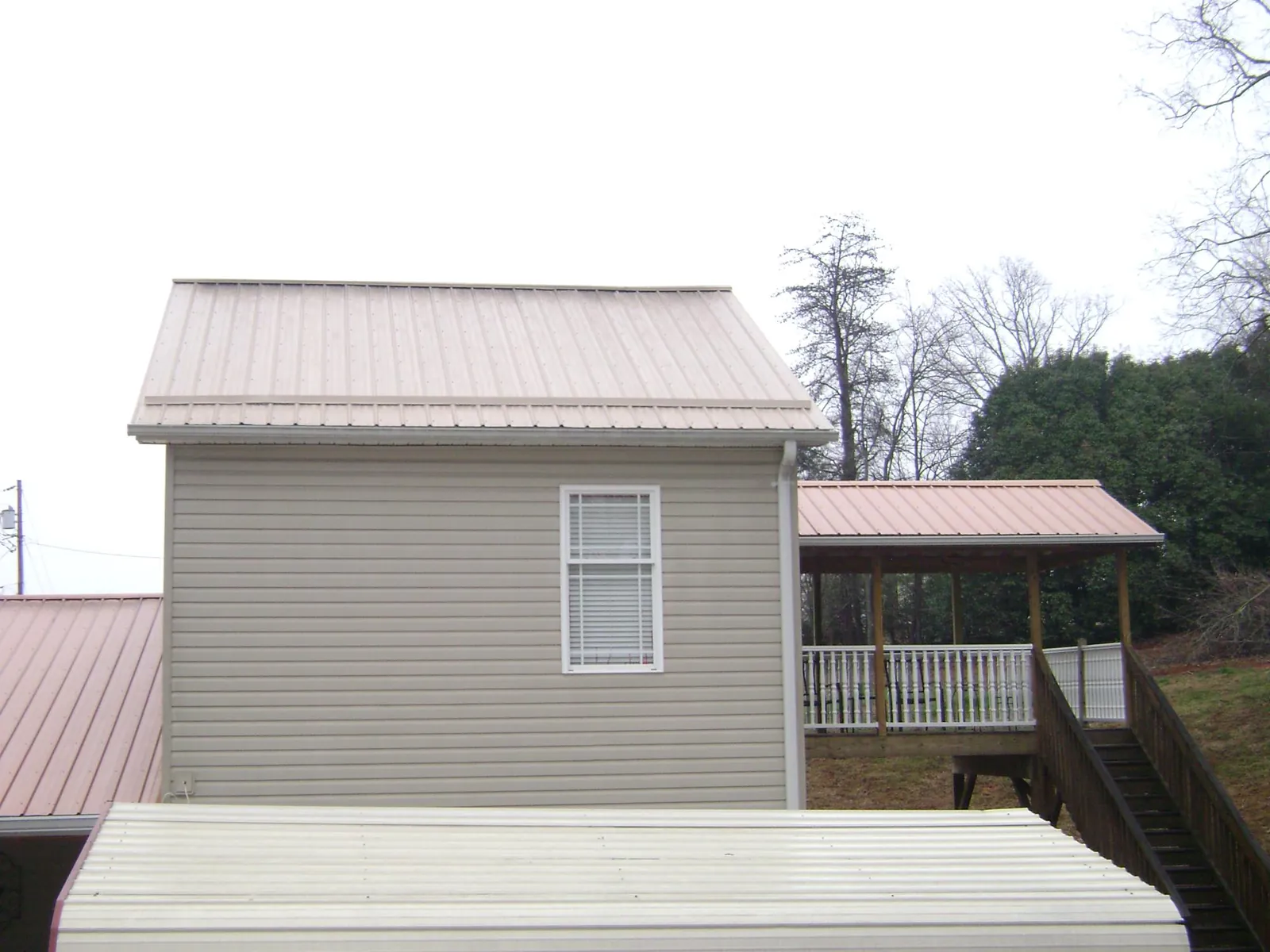Tan metal roofs on a two story addition and attached porch, from a Roof Replacement job in Horntown